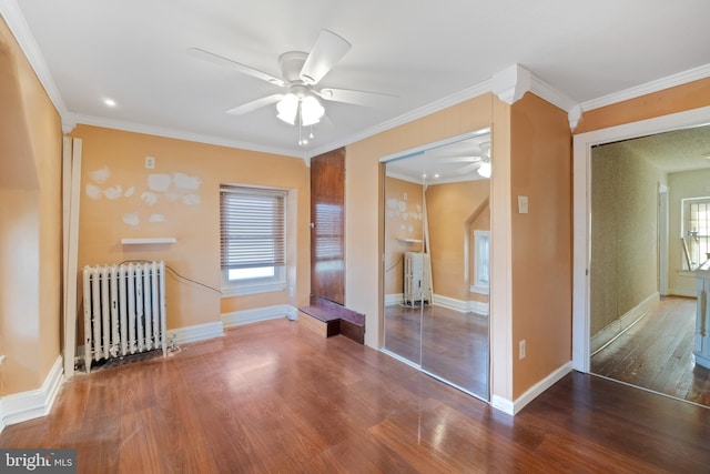 unfurnished bedroom with wood finished floors, radiator heating unit, a closet, crown molding, and baseboards