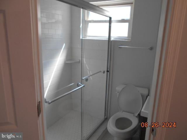 bathroom featuring a shower with shower door and toilet