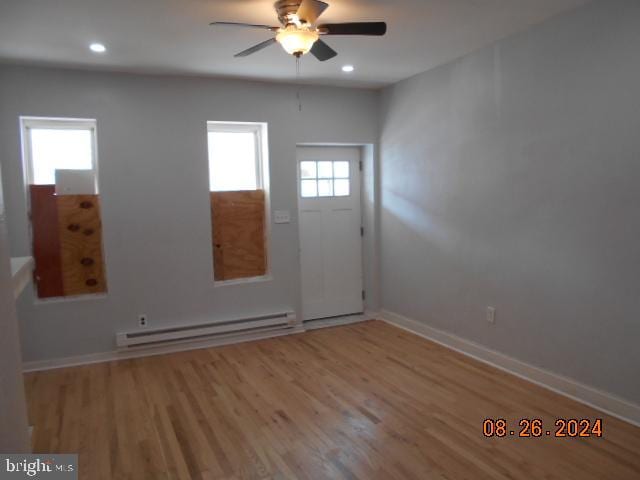 empty room featuring light wood-type flooring, a baseboard heating unit, and plenty of natural light