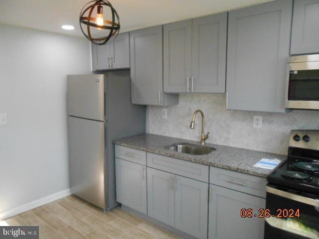 kitchen featuring stainless steel appliances, backsplash, light wood-style floors, a sink, and light stone countertops