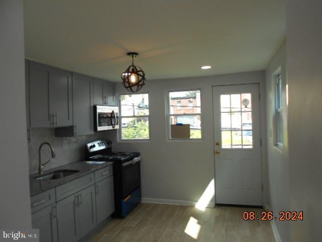 kitchen featuring black range with electric stovetop, decorative backsplash, light hardwood / wood-style floors, sink, and decorative light fixtures