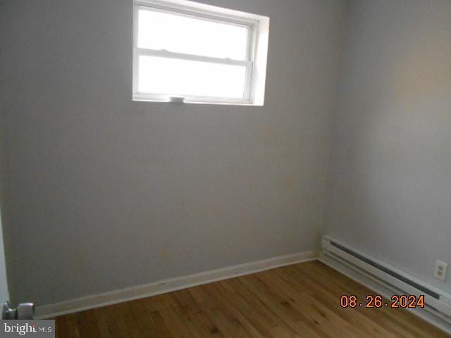 unfurnished room featuring a baseboard radiator, wood finished floors, and baseboards