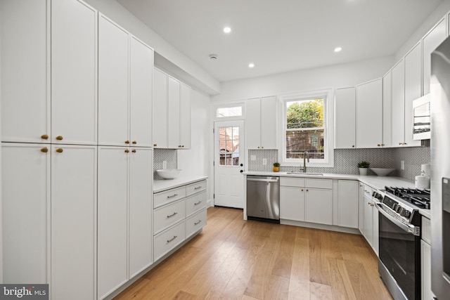 kitchen featuring white cabinetry, sink, light hardwood / wood-style floors, and appliances with stainless steel finishes