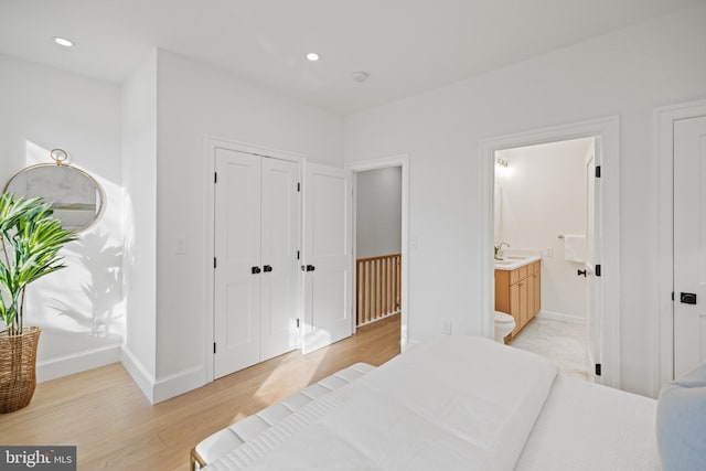 bedroom with connected bathroom, light hardwood / wood-style flooring, and sink