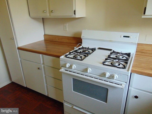 kitchen featuring dark parquet floors, white gas stove, and white cabinetry