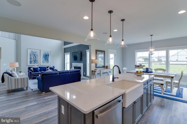 kitchen featuring decorative light fixtures, a large fireplace, stainless steel dishwasher, a kitchen island with sink, and hardwood / wood-style flooring