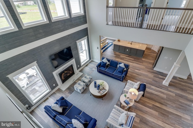 living room featuring a towering ceiling, baseboards, wood finished floors, and a glass covered fireplace