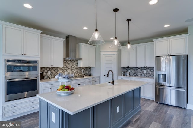 kitchen with stainless steel appliances, wall chimney range hood, a sink, and white cabinets