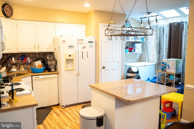 kitchen with white appliances, a skylight, decorative backsplash, decorative light fixtures, and white cabinetry