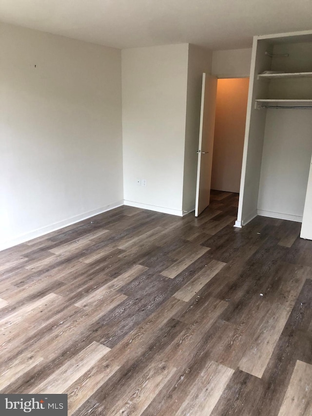 unfurnished bedroom featuring baseboards, dark wood finished floors, and a closet