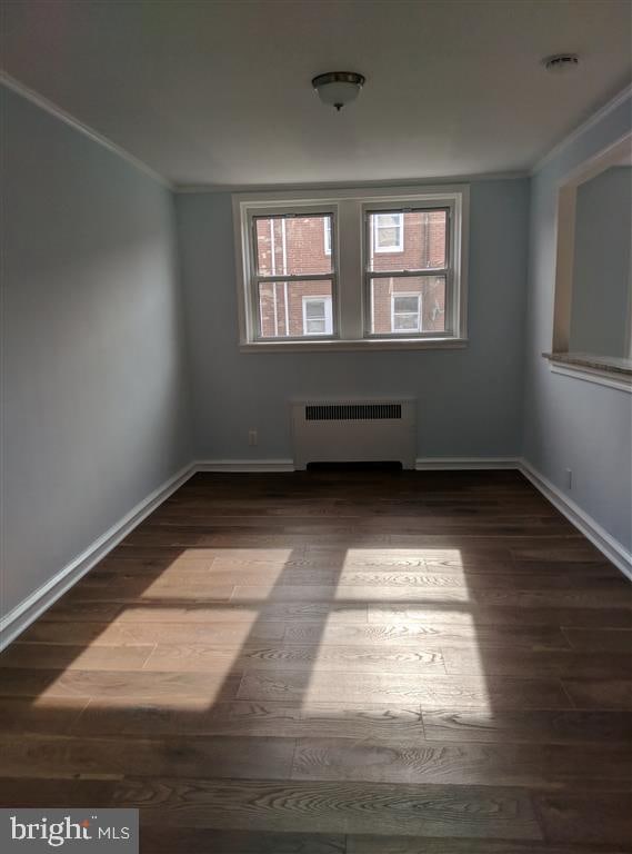 empty room with ornamental molding, radiator, and wood-type flooring