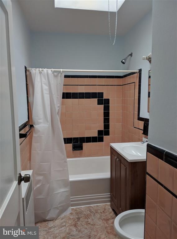 full bathroom featuring toilet, vanity, tile patterned floors, tile walls, and shower / bath combination with curtain