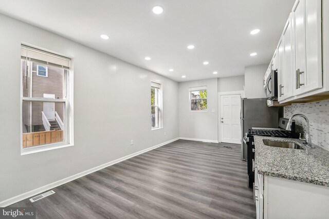 kitchen with light stone countertops, appliances with stainless steel finishes, dark wood-type flooring, sink, and white cabinets