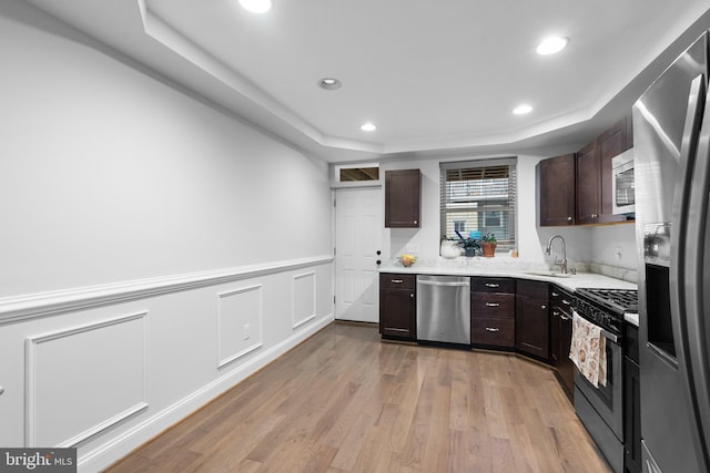 kitchen with appliances with stainless steel finishes, a raised ceiling, sink, and light hardwood / wood-style flooring