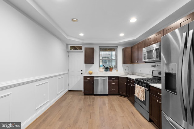 kitchen featuring appliances with stainless steel finishes, light wood-type flooring, sink, and a tray ceiling