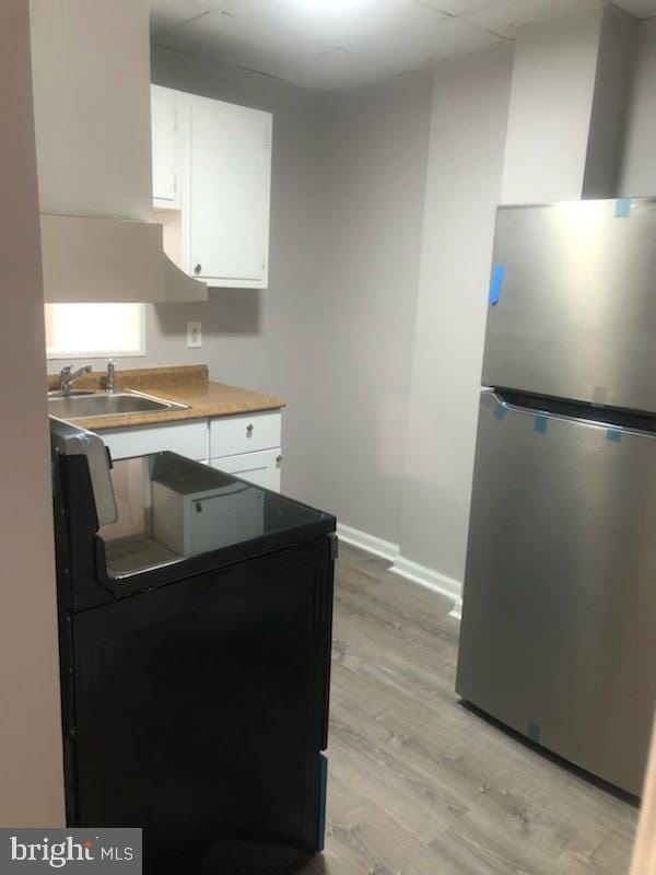 kitchen featuring sink, light wood-type flooring, white cabinets, and stainless steel fridge