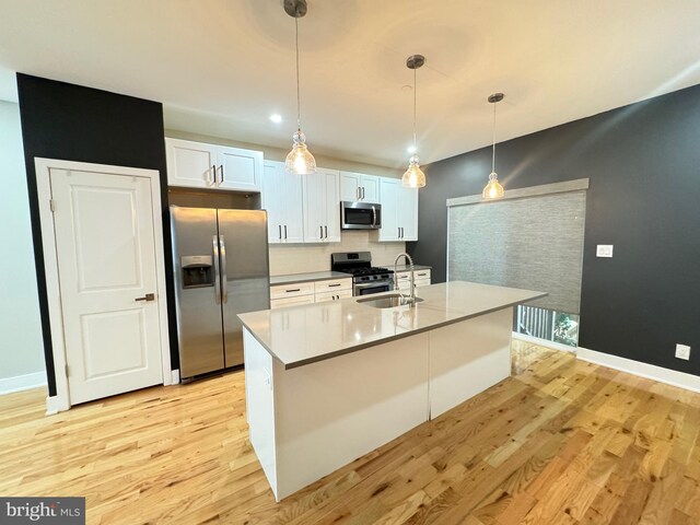 kitchen with pendant lighting, white cabinetry, appliances with stainless steel finishes, light hardwood / wood-style floors, and sink