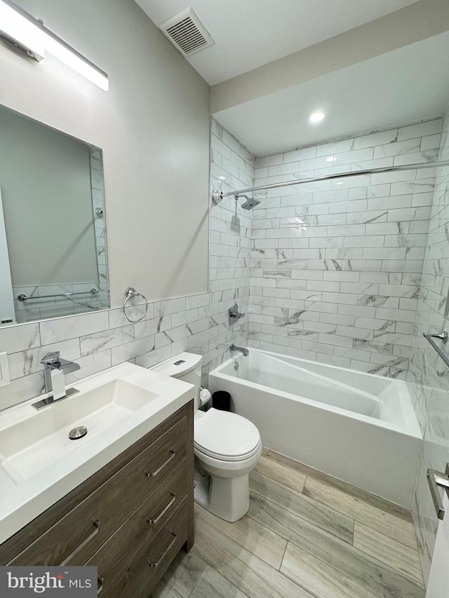 full bathroom featuring tile walls, toilet, tiled shower / bath, and vanity