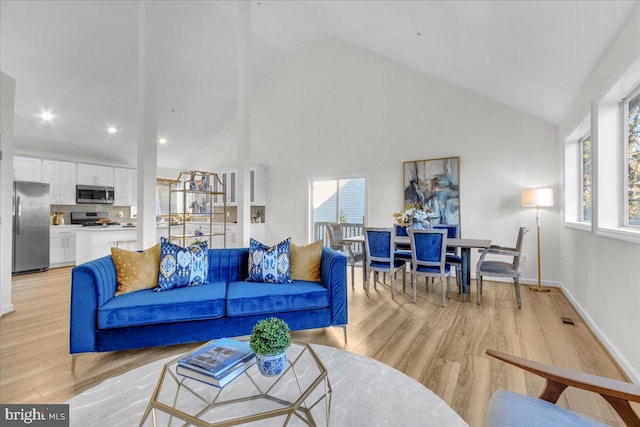 living room featuring high vaulted ceiling, light wood-type flooring, and a healthy amount of sunlight