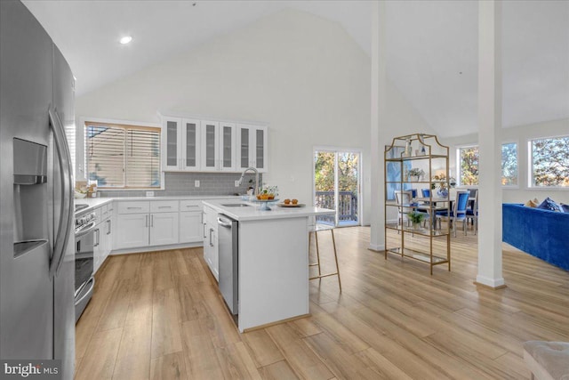 kitchen with stainless steel appliances, an island with sink, light hardwood / wood-style floors, white cabinets, and a kitchen breakfast bar