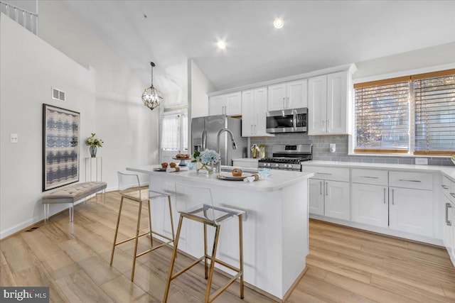 kitchen with stainless steel appliances, a center island with sink, hanging light fixtures, light hardwood / wood-style flooring, and white cabinets