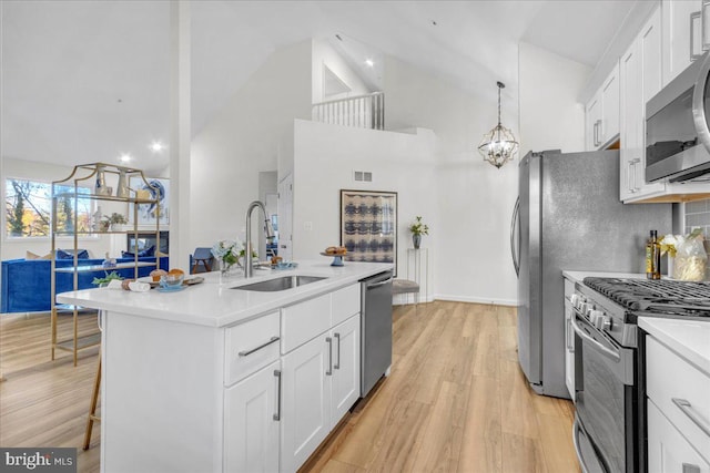 kitchen with light hardwood / wood-style floors, stainless steel appliances, white cabinets, hanging light fixtures, and sink