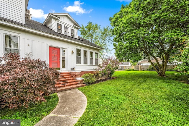 view of front of house featuring a shingled roof, fence, and a front lawn