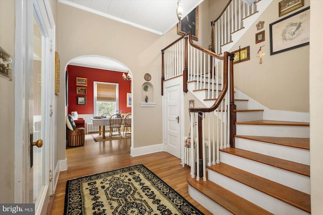 foyer entrance with arched walkways, ornamental molding, wood finished floors, baseboards, and stairs