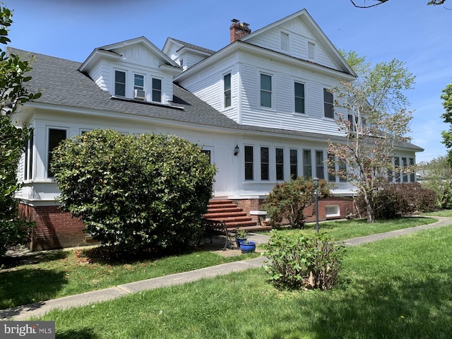 view of front of home featuring brick siding, a chimney, a front lawn, and roof with shingles