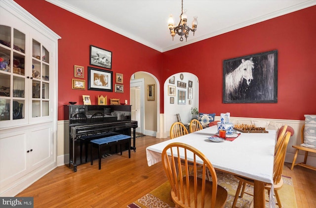 dining room featuring ornamental molding, arched walkways, a notable chandelier, and wood finished floors