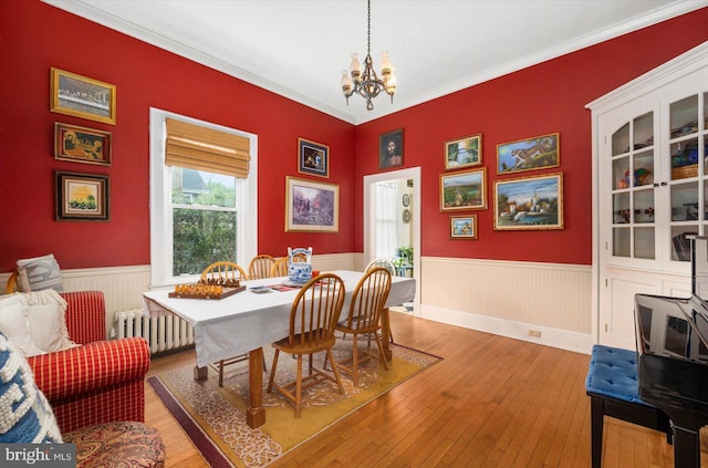 dining area featuring a chandelier, a wainscoted wall, light wood finished floors, and radiator heating unit