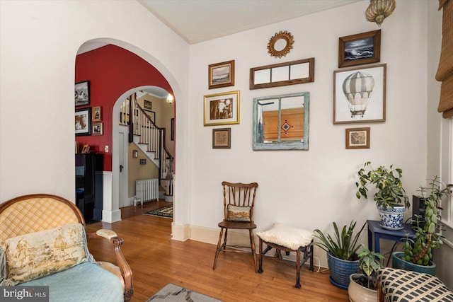 living area with arched walkways, radiator heating unit, wood finished floors, stairs, and crown molding