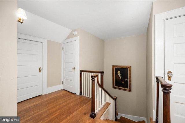 hall with baseboards, vaulted ceiling, wood finished floors, and an upstairs landing