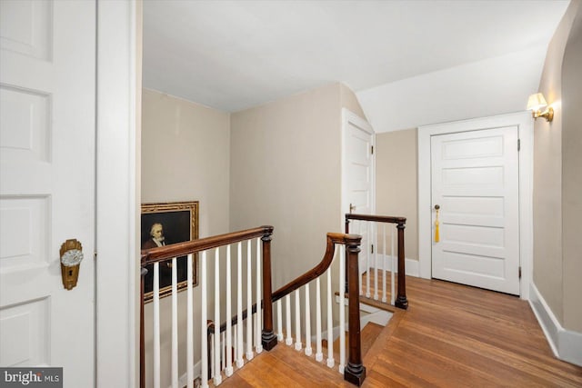 corridor with baseboards, wood finished floors, and an upstairs landing