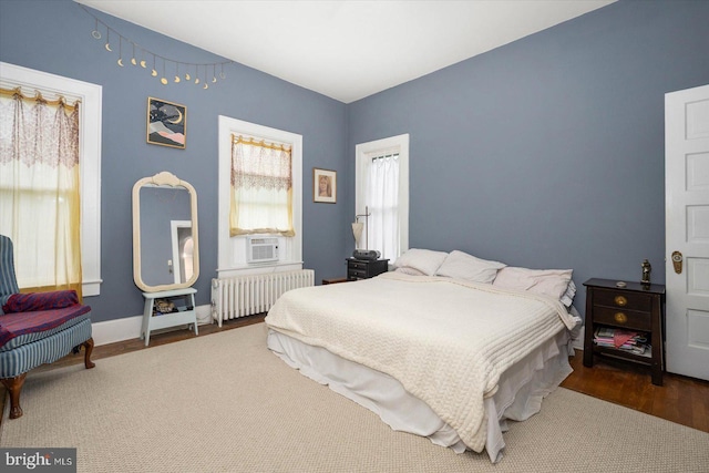 bedroom with radiator heating unit, cooling unit, wood finished floors, and baseboards