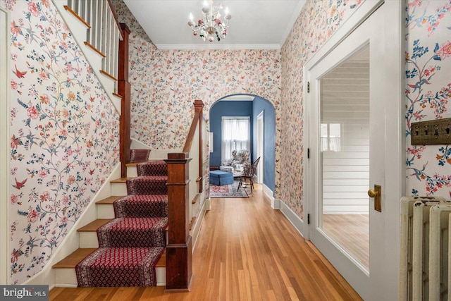 stairs featuring arched walkways, wood finished floors, ornamental molding, radiator, and wallpapered walls