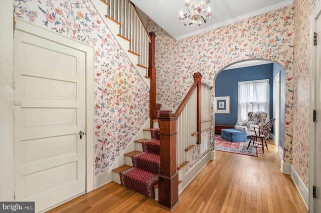 stairway featuring wallpapered walls, arched walkways, wood finished floors, and ornamental molding