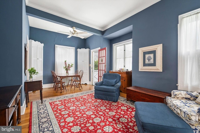 living room featuring ceiling fan, crown molding, baseboards, and wood finished floors