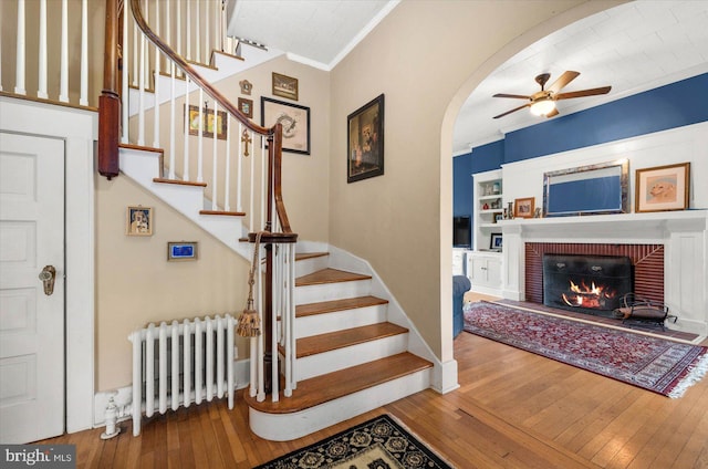 staircase with radiator, ornamental molding, arched walkways, and wood finished floors