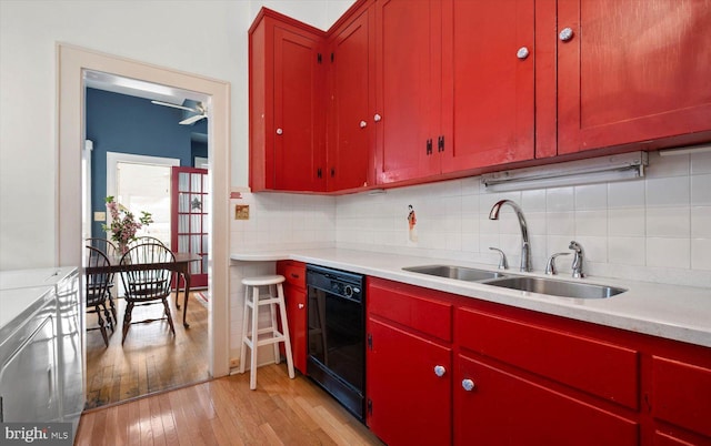 kitchen with dishwasher, backsplash, light countertops, light wood-type flooring, and a sink