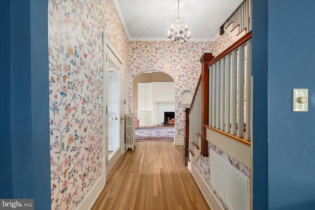 hall featuring wood finished floors, crown molding, baseboards, and wallpapered walls