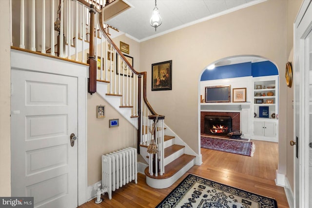 foyer entrance featuring radiator, stairway, ornamental molding, a brick fireplace, and wood finished floors