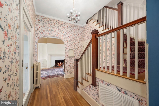 interior space featuring wood finished floors, baseboards, ornamental molding, radiator, and wallpapered walls