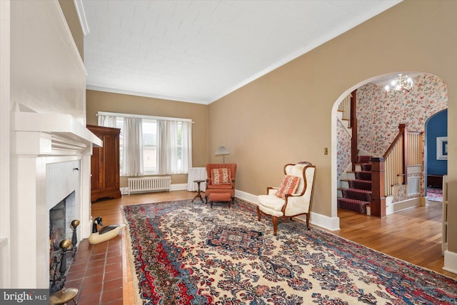 living area featuring crown molding, stairway, arched walkways, and radiator