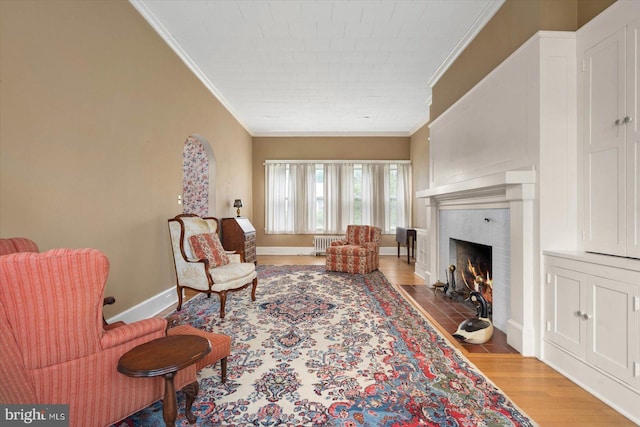 living area with baseboards, radiator heating unit, a fireplace with flush hearth, wood finished floors, and crown molding