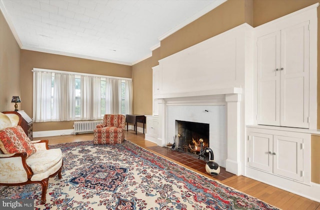 living area with a fireplace with flush hearth, baseboards, ornamental molding, radiator, and dark wood-style floors