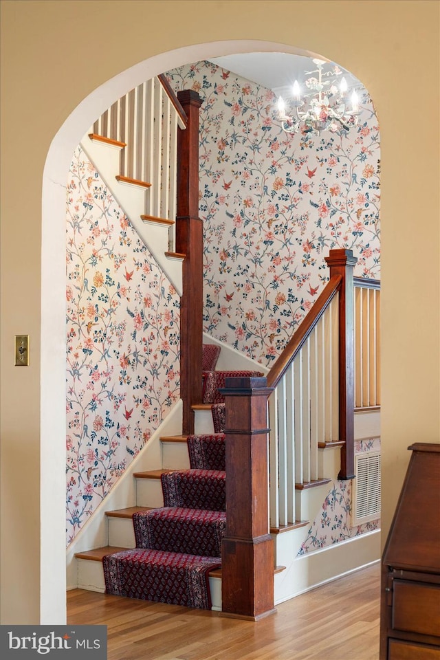 stairs with wood finished floors and a notable chandelier