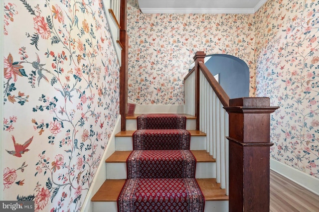 staircase with wallpapered walls, baseboards, crown molding, and wood finished floors