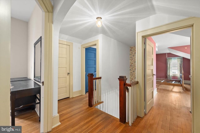 hall with vaulted ceiling, light wood finished floors, and an upstairs landing