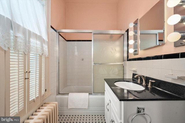 bathroom featuring tile walls, radiator, combined bath / shower with glass door, and vanity